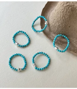 Detail view of five turquoise beaded rings with S925 silver accents on a textured surface