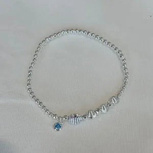 Close-up of S925 silver beaded bracelet with blue gem charm and shell bead detail