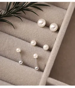 Close-up detail of 925 silver pearl stud earrings in a beige velvet jewelry tray
