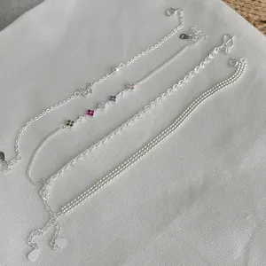 Close-up of four distinct silver-tone chain bracelets with delicate charms and textures