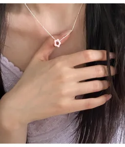 Close-up of a 925 silver necklace with a dainty pink flower pendant on a model.