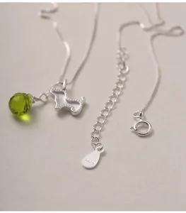 Macro view of S925 sterling silver necklace featuring cute dog and green crystal drop.