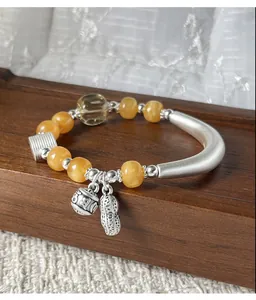 Detailopname van de zilveren pinda-bedel en doorschijnende barnsteen kralen aan armband