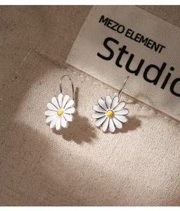 Detalle de pendientes de margarita de plata de ley blancos y amarillos sobre un fondo de tela