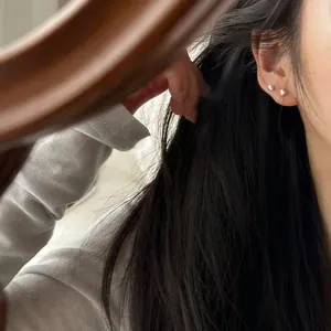 Detail view of minimalist 990 sterling silver small stud earrings on female ear