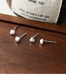 Close-up of matte silver stud earrings in heart and square shapes on dark wooden base
