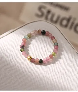 Close-up of a handmade tourmaline beaded ring with a gold accent bead on white texture.