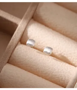 Detailed close-up of matte 990 sterling silver square stud earrings in jewelry box