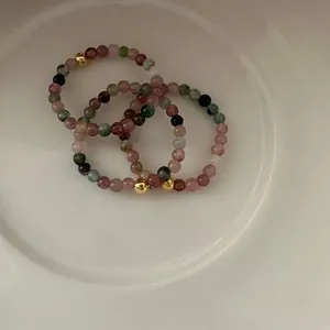 Close-up of tourmaline beaded elastic rings with small gold beads on white plate