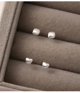 Close-up detail of matte sterling silver heart and square stud earrings in a velvet box