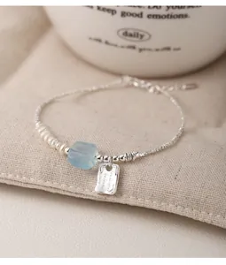 Macro shot of silver bracelet featuring white pearls and faceted light blue gemstone charm