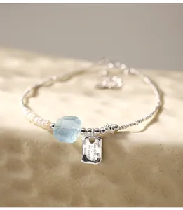 Detailed view of a 925 sterling silver pearl bracelet with aquamarine and engraved charm
