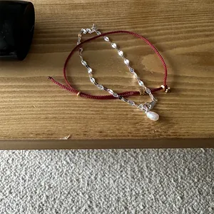 Detail view of 925 sterling silver chain and red woven bracelet with a pearl pendant