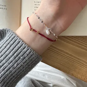 Close-up of stackable 925 sterling silver pearl bracelet and red woven coin hand rope
