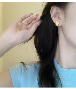 Detail view of irregular gold-plated square stud earrings with pearl inlay worn on ear
