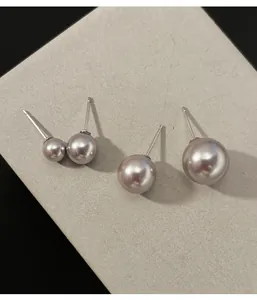 Close-up of elegant round grey pearl stud earrings on a textured off-white display card.