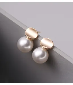 Close-up detail of elegant gold-tone irregular disc and white pearl stud earrings for women