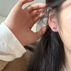 Detail showing a tiny heart-shaped silver stud with blue zircon on a woman's ear