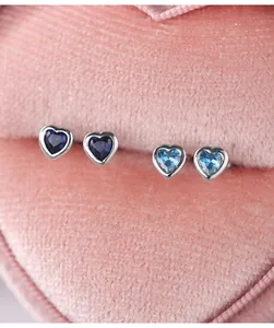 Macro view of blue and light blue heart-shaped silver stud earrings in a pink velvet box.