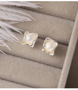 Detailed macro view of irregular silver square stud earrings with elegant white pearls.