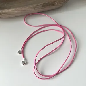 Detailed view of long pink suede cord necklace with polished silver heart charms