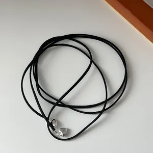 Detailed view of a long black cord necklace with two polished silver heart pendants
