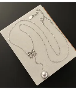 Detail of silver bow necklace with a shimmering pearl drop on a gray display.