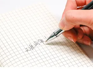 Close-up of a premium metal rollerball pen writing smooth ink on a grid notebook.