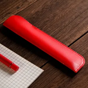 Elegante custodia per penne in pelle rossa su scrivania in legno con quaderno a quadretti