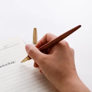 Bolígrafo de gel de sándalo vintage con detalles de latón sostenido por una mano escribiendo