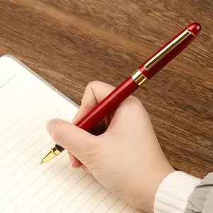 Professional redwood rollerball pen with gold accents held in hand over a notebook