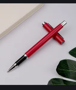 Detailed view of a sleek red metal rollerball pen with chrome accents on a minimalist desk.