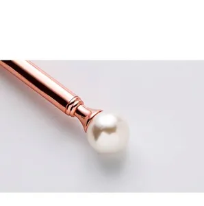 Close-up of elegant rose gold metal ballpoint pen featuring a large pearl top detail.