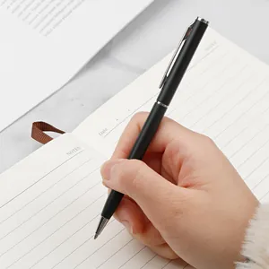 Hand hält einen eleganten schwarzen Kugelschreiber aus Metall über einem Notizbuch.
