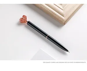 Detail eines schwarzen Metall-Kugelschreibers mit roségoldenem hohlem Herz-Aufsatz.