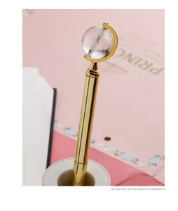 Detail view of a golden metal ballpoint pen featuring a clear crystal globe topper design