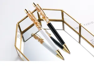 Close-up of floating gold foil inside elegant black and white metal ballpoint pens.