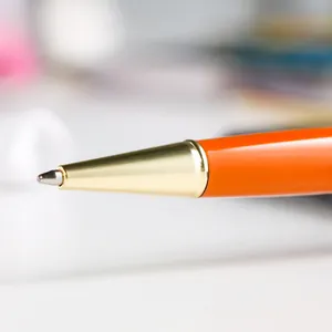 Close-up macro shot of a metallic orange ballpoint pen featuring a polished gold-tone tip