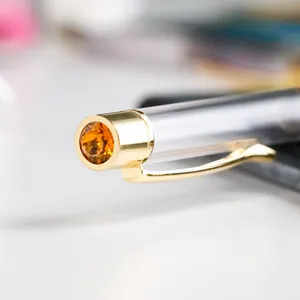 Elegant gold metal ballpoint pen with a large amber rhinestone on the faceted cap