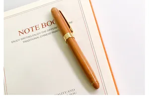 Close-up detail of an elegant wooden fountain pen with gold trim resting on a white notebook