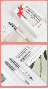 Detail showing stylish metal ballpoint pens with floral patterns and white gift box packaging.