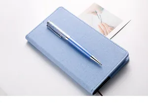 Nahaufnahme eines blauen Metall-Kugelschreibers mit funkelnder Kristallspitze auf Notizbuch