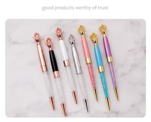Detail view of seven assorted crown-topped metal ballpoint pens on white marble surface.