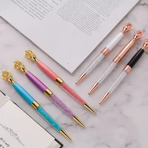 Elegant metal ballpoint pens with crown toppers and crystal filling on marble surface