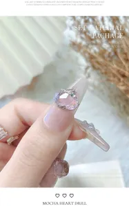 Detailopname van een roze hartvormige kristallen nagelkunstbedel met zilveren rand