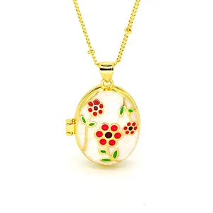 Close-up of an oval gold locket necklace with red and green enamel flower patterns