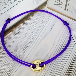 Close-up of a purple adjustable string bracelet featuring a gold pig nose charm