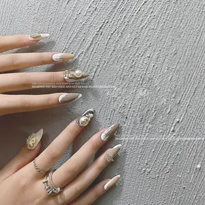 Elegant pearl and bow nail charms on manicured nails with a textured gray backdrop.