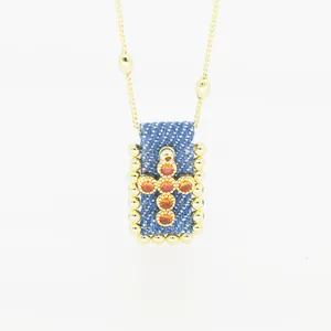 Dettaglio del ciondolo a croce in denim bohémien con zirconi arancioni e catena