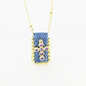 Dettaglio squisito della collana a croce bohémien con zirconi viola su un ciondolo in denim blu
